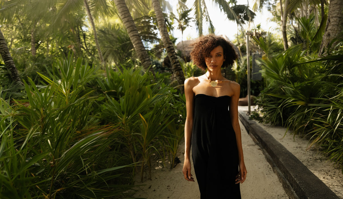 Vestido Bruma negro de La Troupe, vestido largo sin tirantes en una sesión editorial entre palmeras.