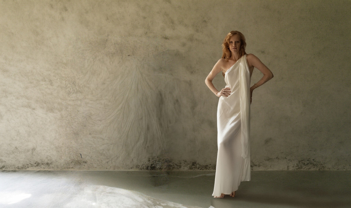 Vestido Ondina Seda blanco de La Troupe, diseño largo asimétrico de un hombro con caída fluida en interior de tonos neutros.